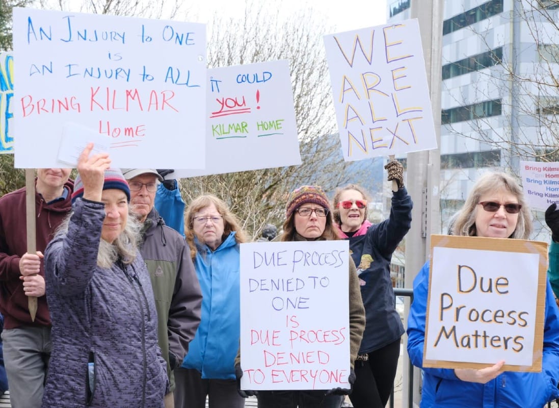 A photo of a group of protesters holding signs. Some of the signs contain light text that is hard to read. There is only one sign that is easy to read because the letters are dark and large. It reads, "Due Process Matters".